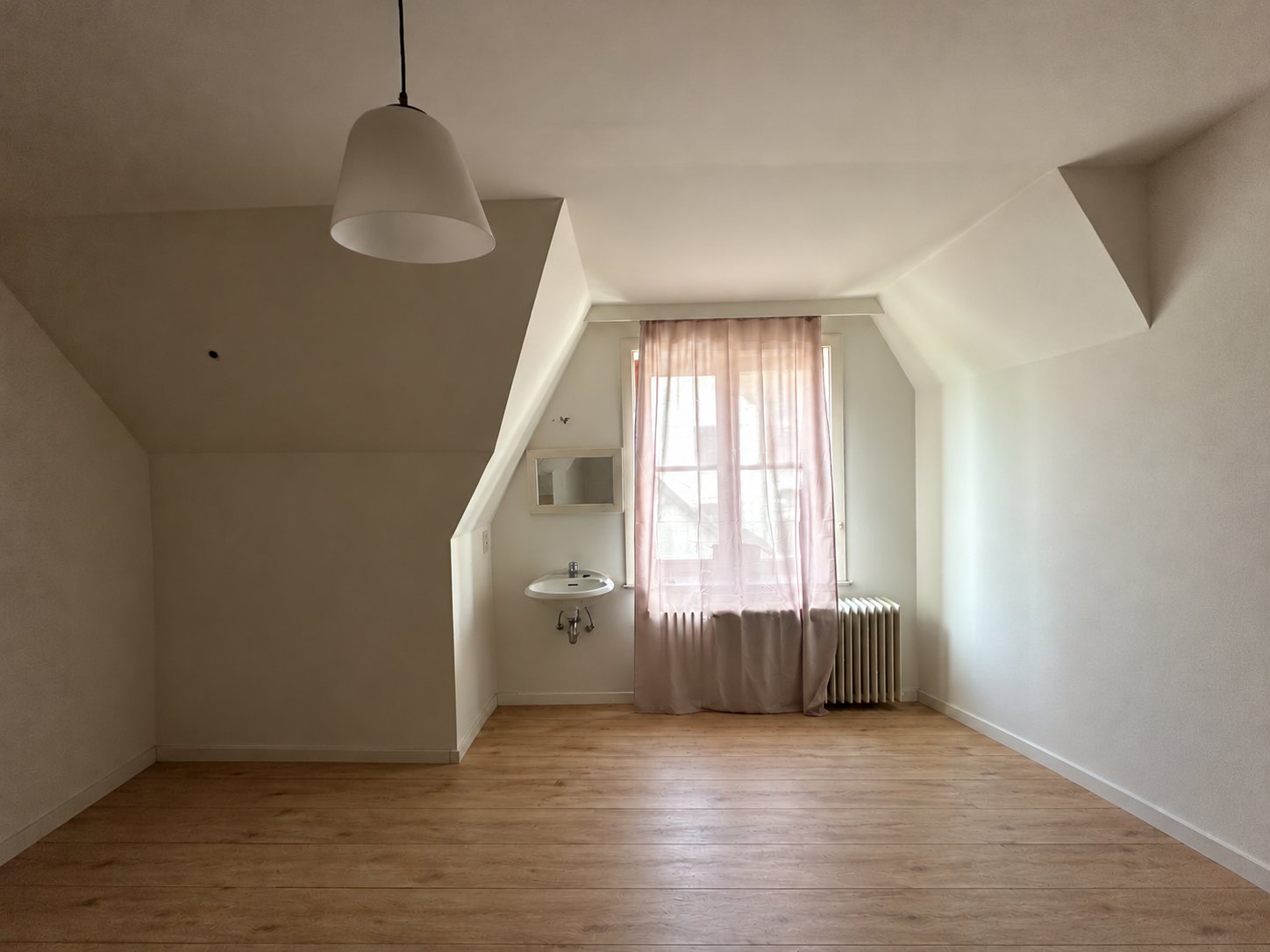 De lege kamer onder het schuine dak met raam en wastafel